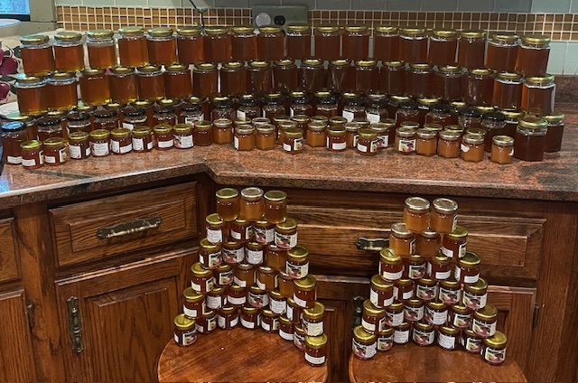 Rows of filled honey jars stacked across a kitchen counter